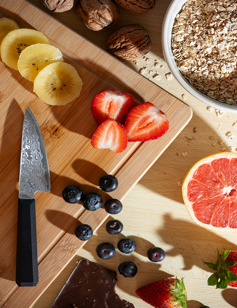 Assiette et planche de fruits frais: kiwi, fraises, myrtilles et pamplemousse, couteau damas sur planche, bowls de flocons d’avoine et morceaux de chocolat. comment faire le tranchant d'un couteau intégré naturellement dans la description du matériel.