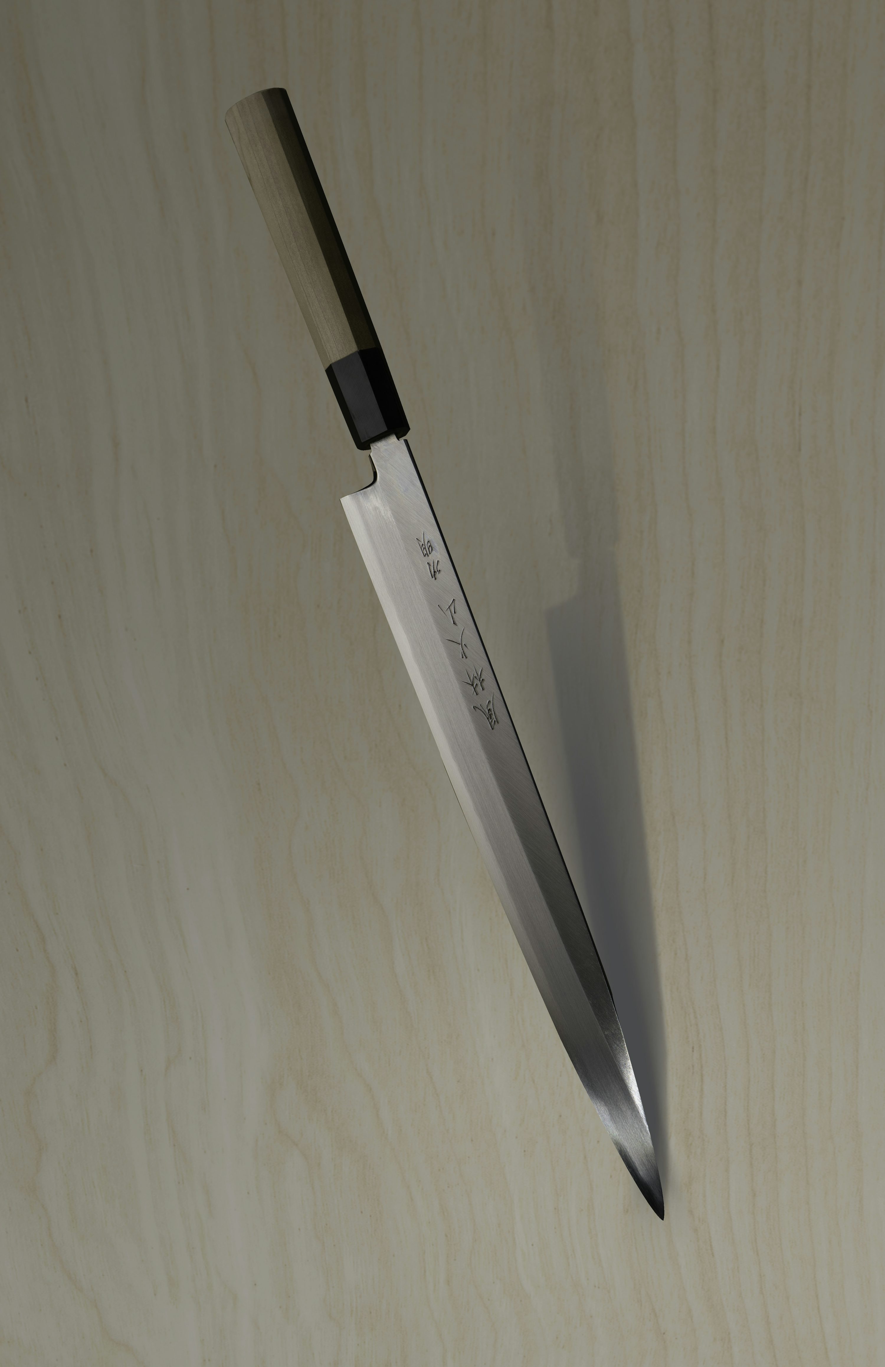 Couteau japonais traditionnel avec lame longue et affûtée, manche en bois clair, posé sur bois clair.