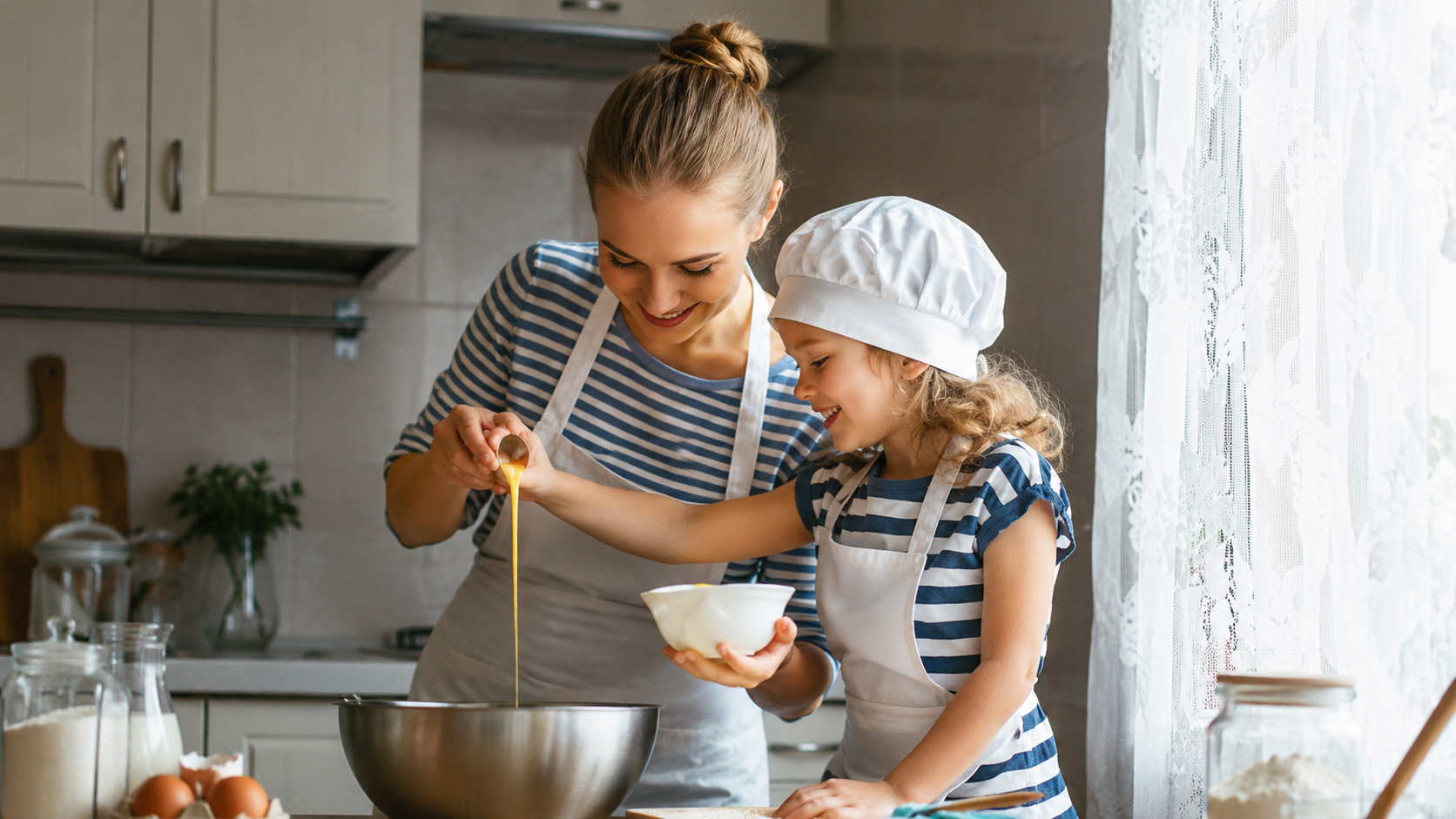 Mère et fille en cuisine, préparant ensemble une pâte dans un grand bol, fille porte un toque blanche.