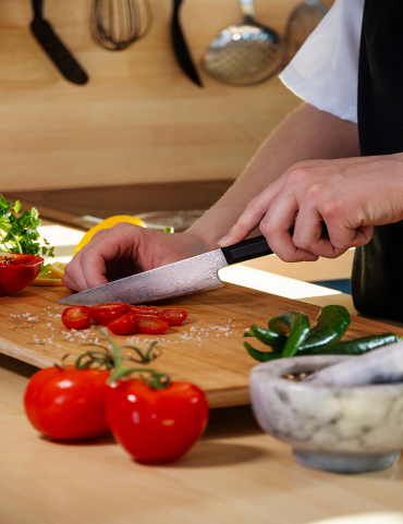 Une personne coupe des tomates sur une planche de cuisine avec un couteau.